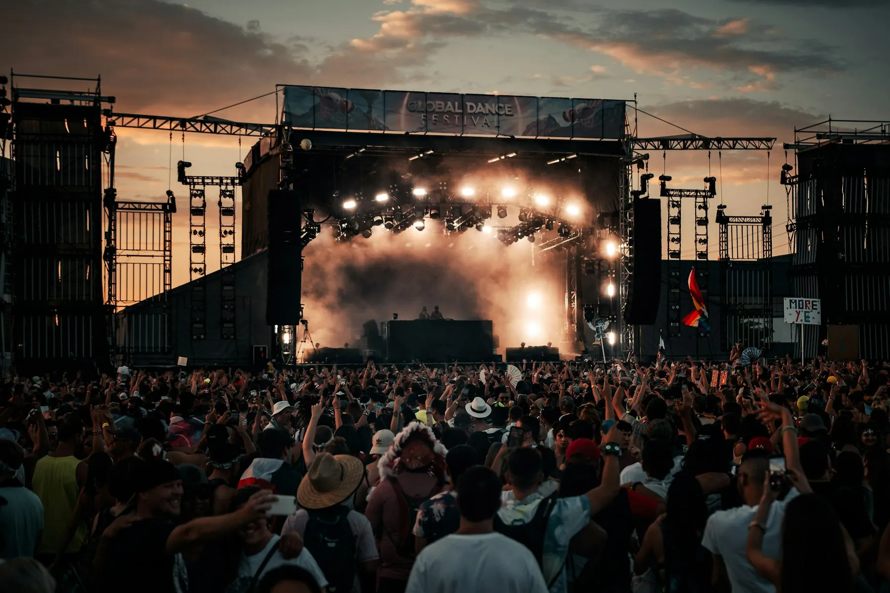 Palco principal de festival com torres de som, estrutura de iluminação e multidão
